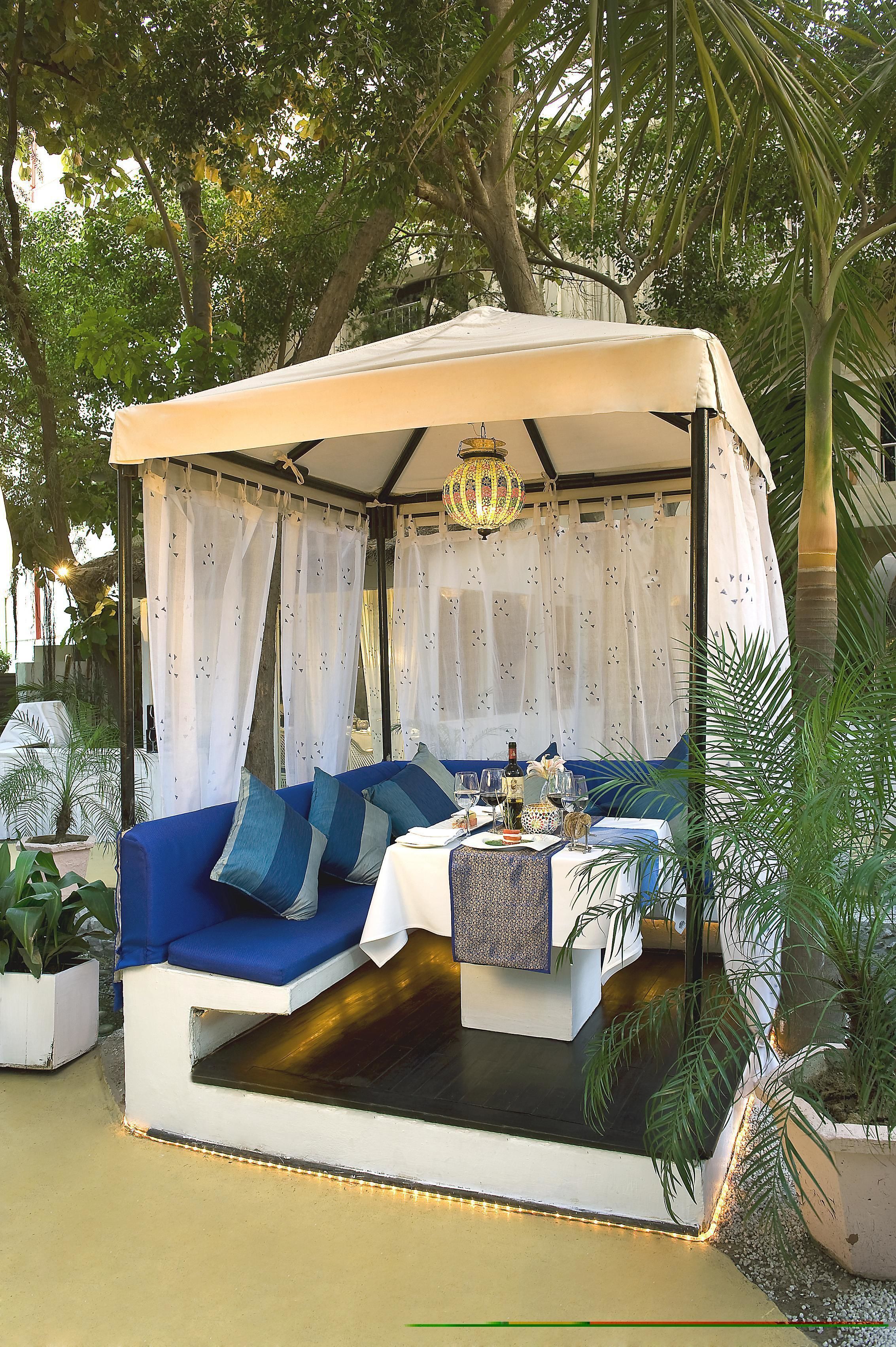 A covered outdoor seating area with a sofa and table, surrounded by greenery.