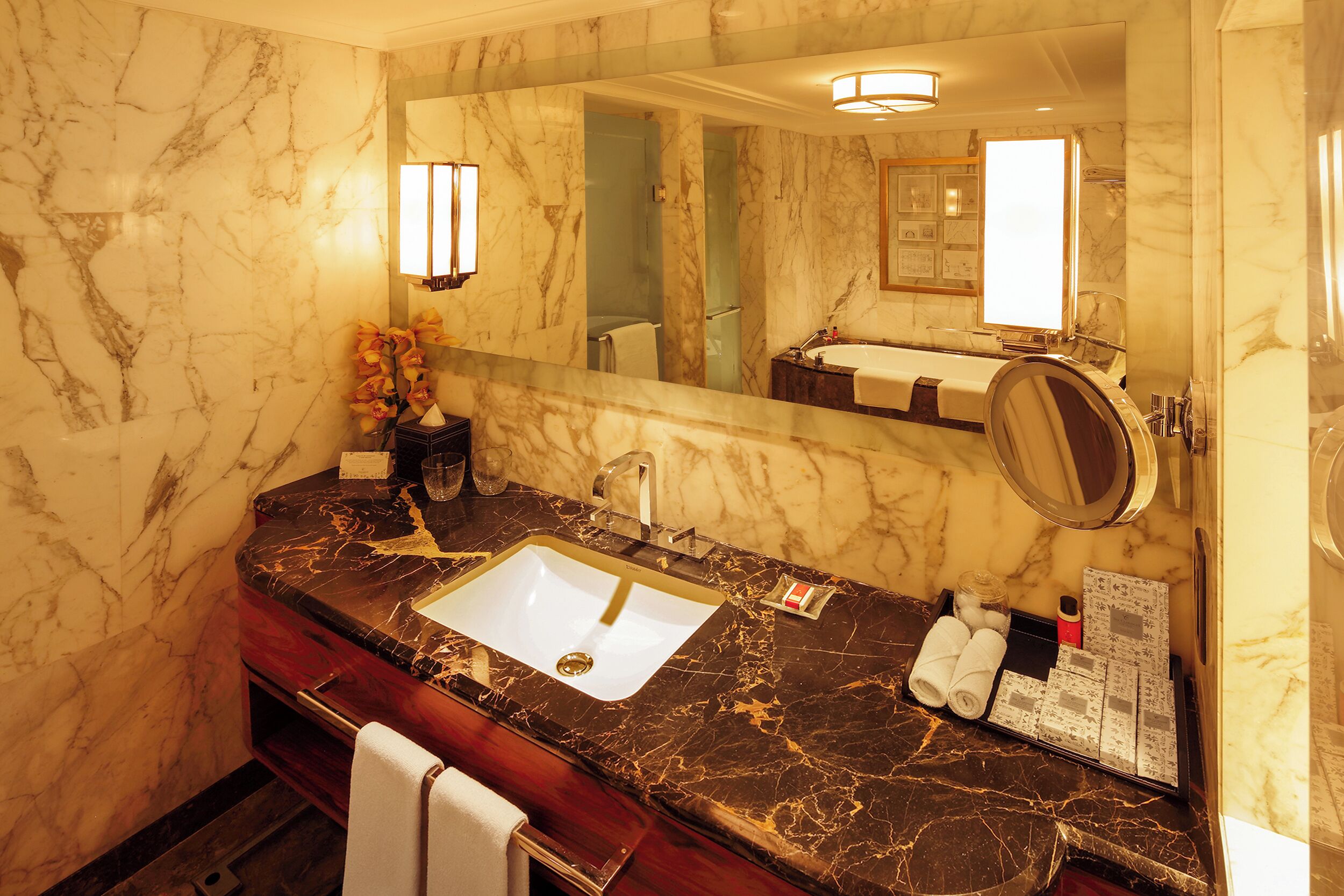 A bathroom with a marble wall, a sink, a mirror, and a towel rack.