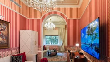 Una habitación con papel tapiz a rayas, un candelabro, un sofá, un televisor y una ventana con vistas a árboles.