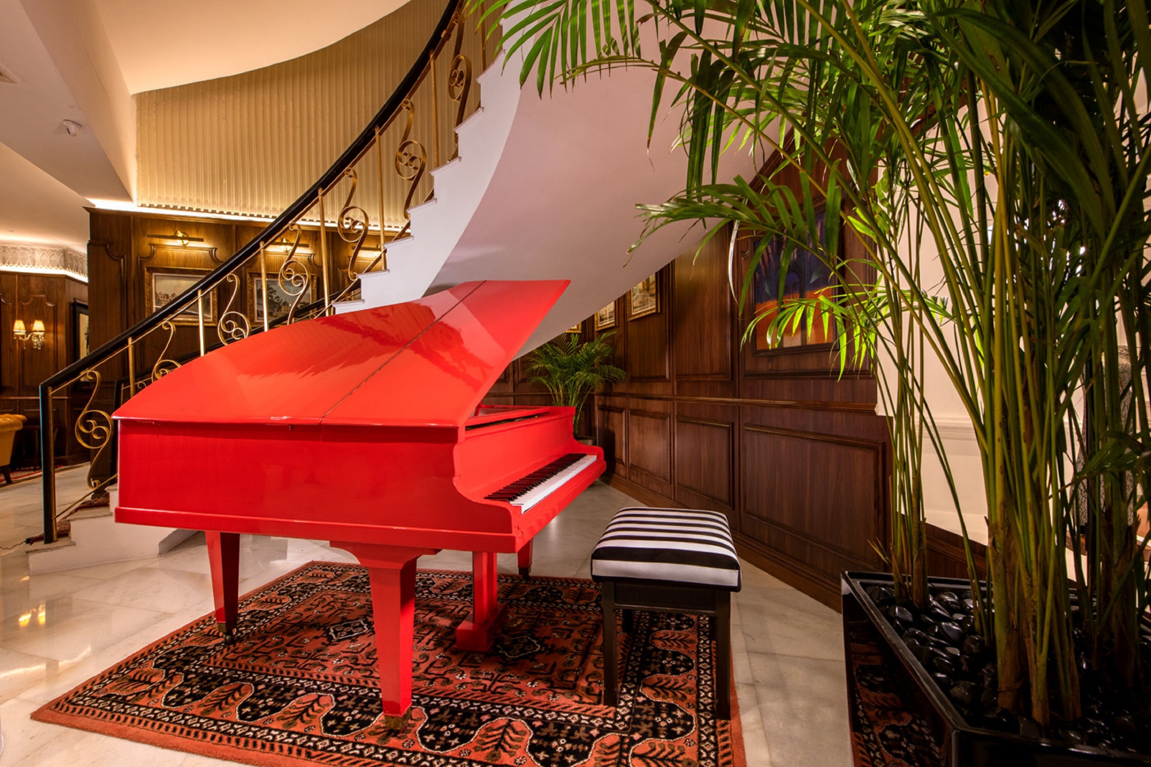 A grand piano in a spacious lobby with a marble floor, a staircase, and a large potted plant.