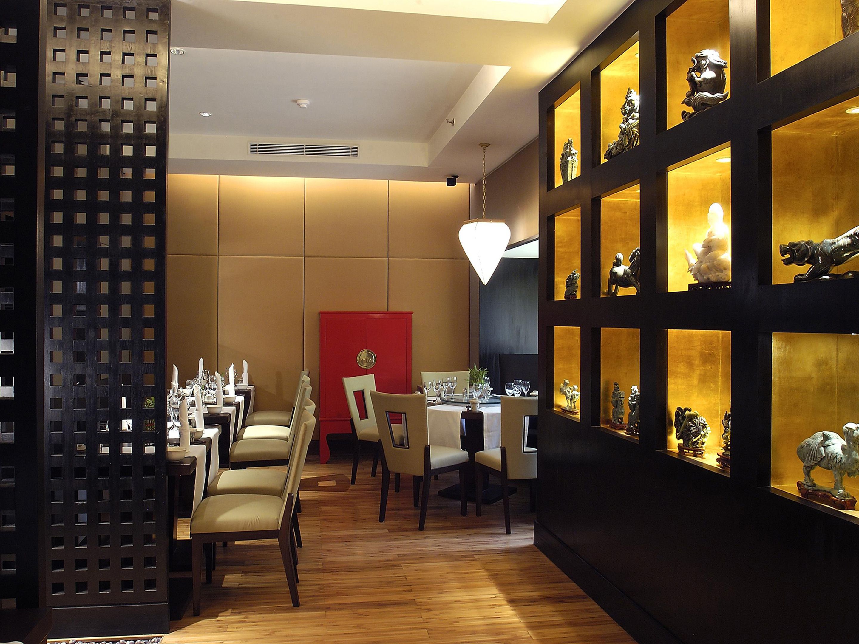 A dining area with wooden flooring, tables, chairs, and a red accent wall.