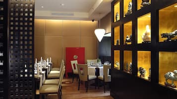 A dining area with wooden flooring, tables, chairs, and a red accent wall.