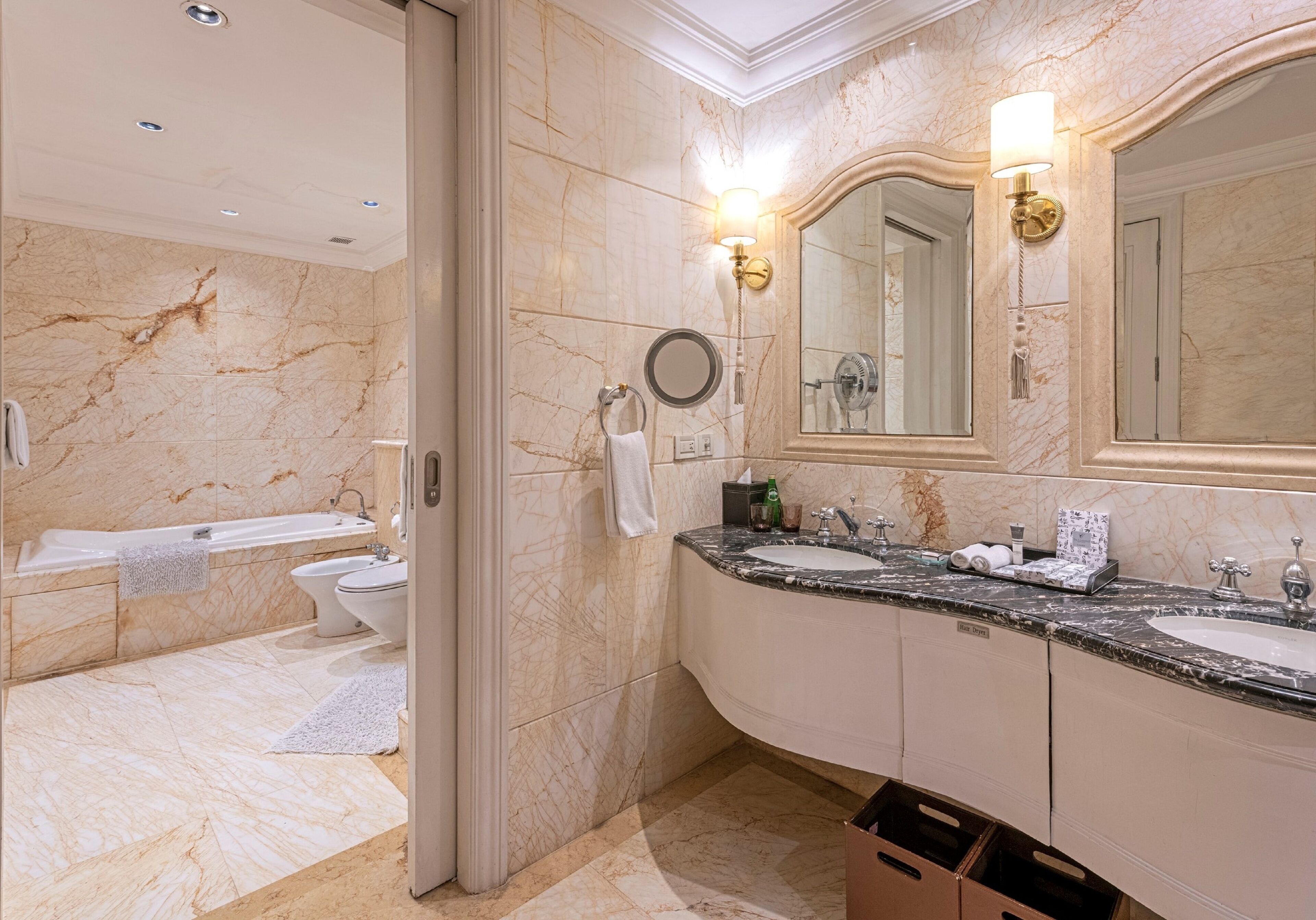 Un baño moderno con suelo de mármol, una bañera, un inodoro, un lavabo y un espejo grande.