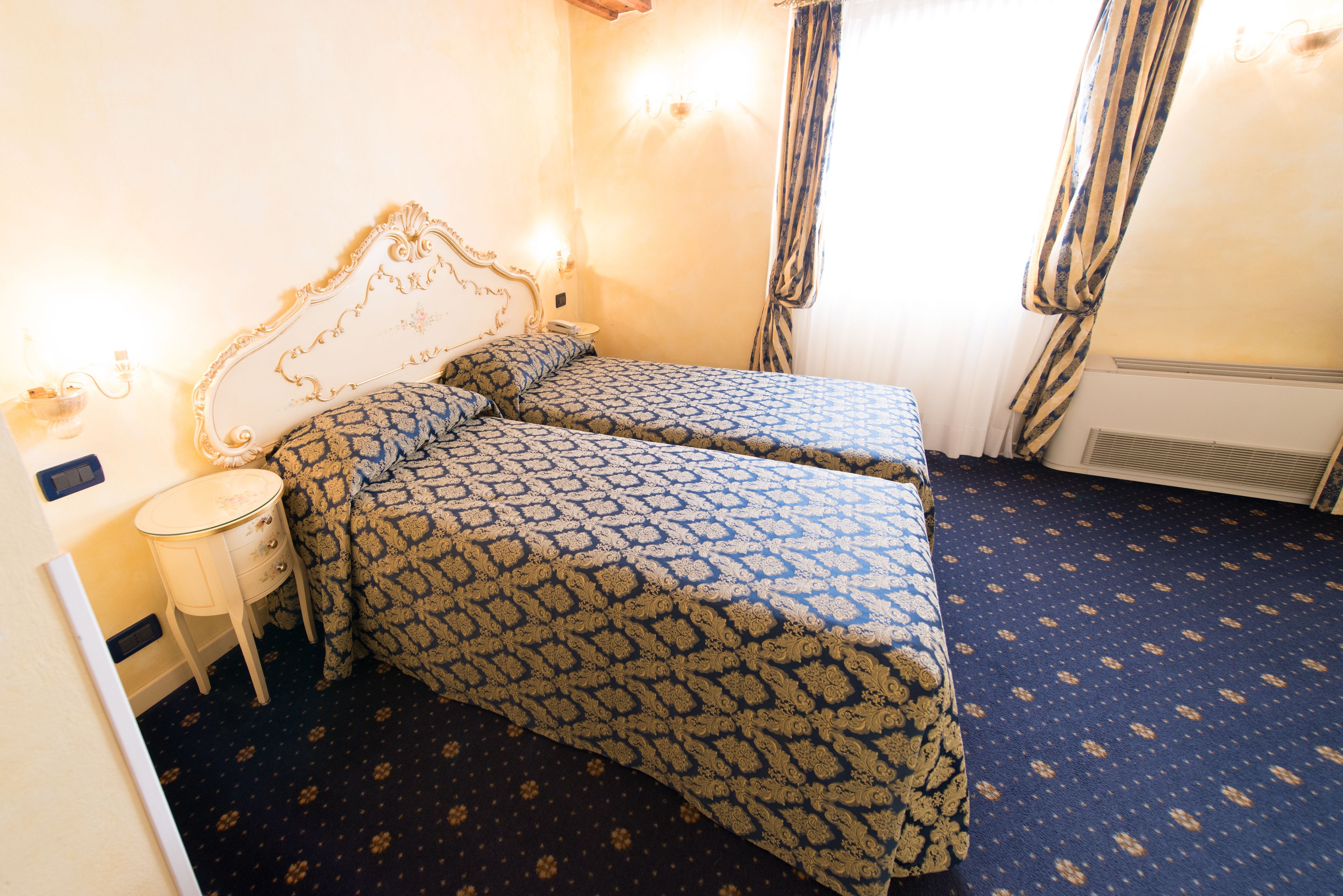 A bedroom with two beds, a bedside table, and a window with curtains.