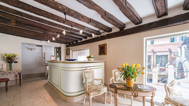 A room with a bar area, two chairs, a table with a vase of flowers, and a view of the outside. - Locanda Ca' Zose (Venice)