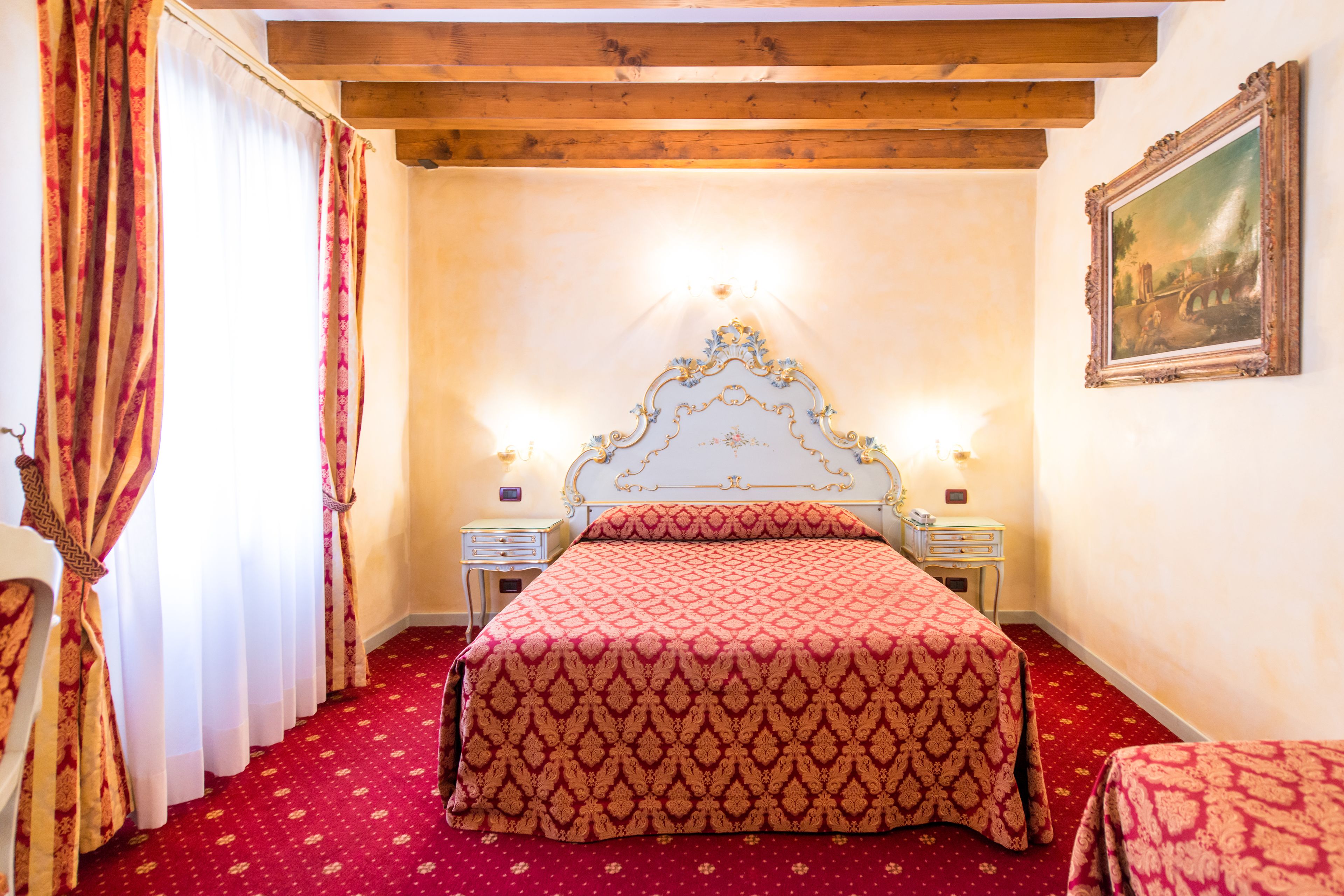 A bedroom with a large bed, two bedside tables, a nightstand, a red carpet, and a wooden ceiling.