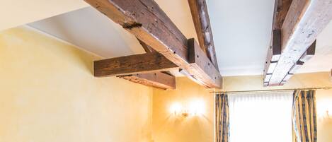 A bedroom with two beds, wooden beams, a patterned bedspread, and a window with curtains.