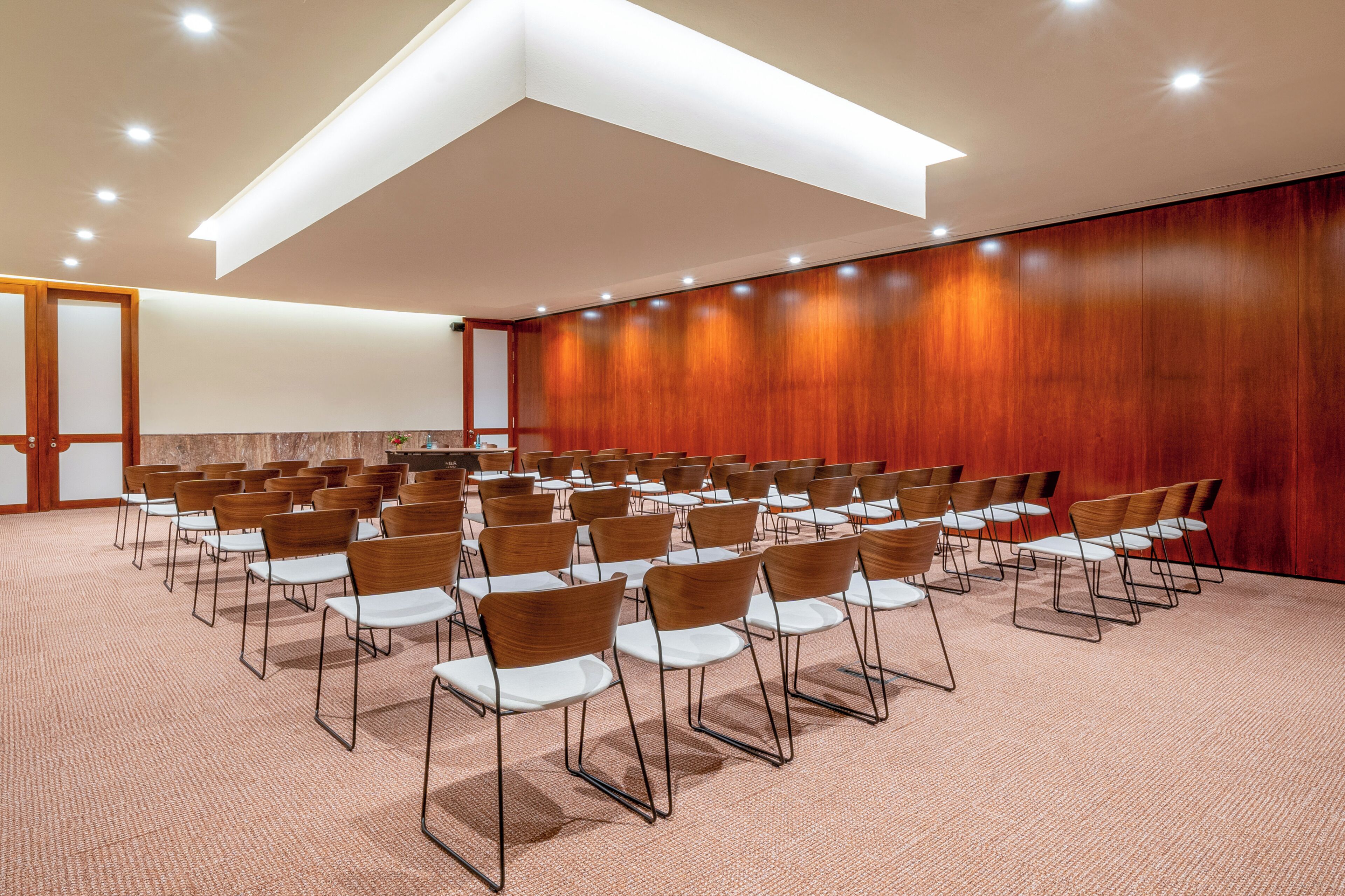 Un salón de conferencias con filas de sillas, una pared de madera y piso alfombrado.