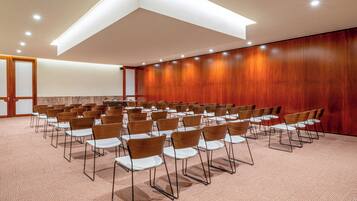 Un salón de conferencias con filas de sillas, una pared de madera y piso alfombrado.