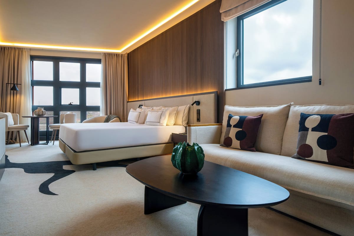A modern hotel room with a large bed, a sofa, a coffee table, and a desk.