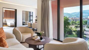 Habitación de hotel moderna con un amplio ventanal que ofrece vistas a la ciudad, un espacio de descanso acogedor y un dormitorio bien amoblado.