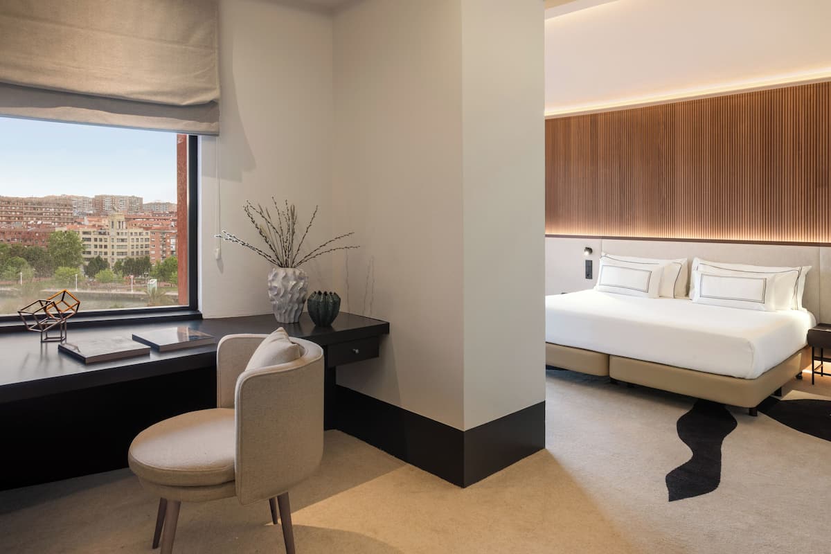 A modern hotel room with a desk, chair, and a large bed with a headboard.
