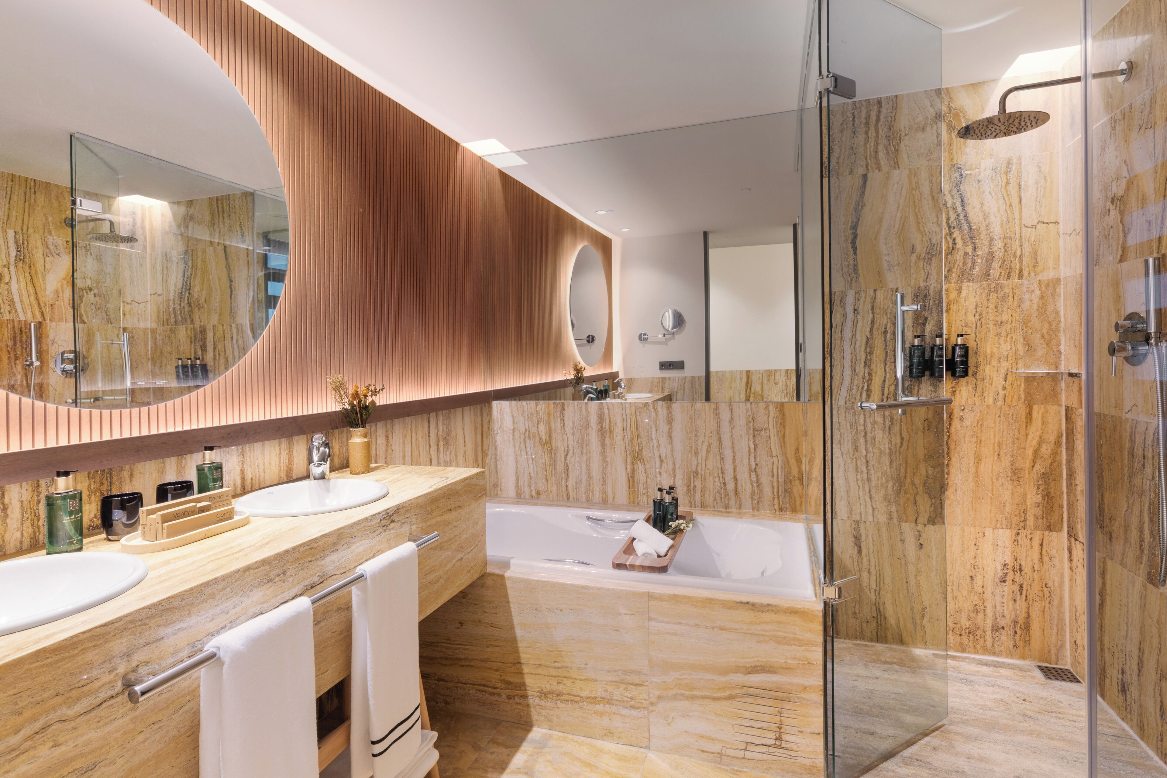 A modern bathroom with a large mirror, two sinks, a bathtub, and a glass-enclosed shower area.