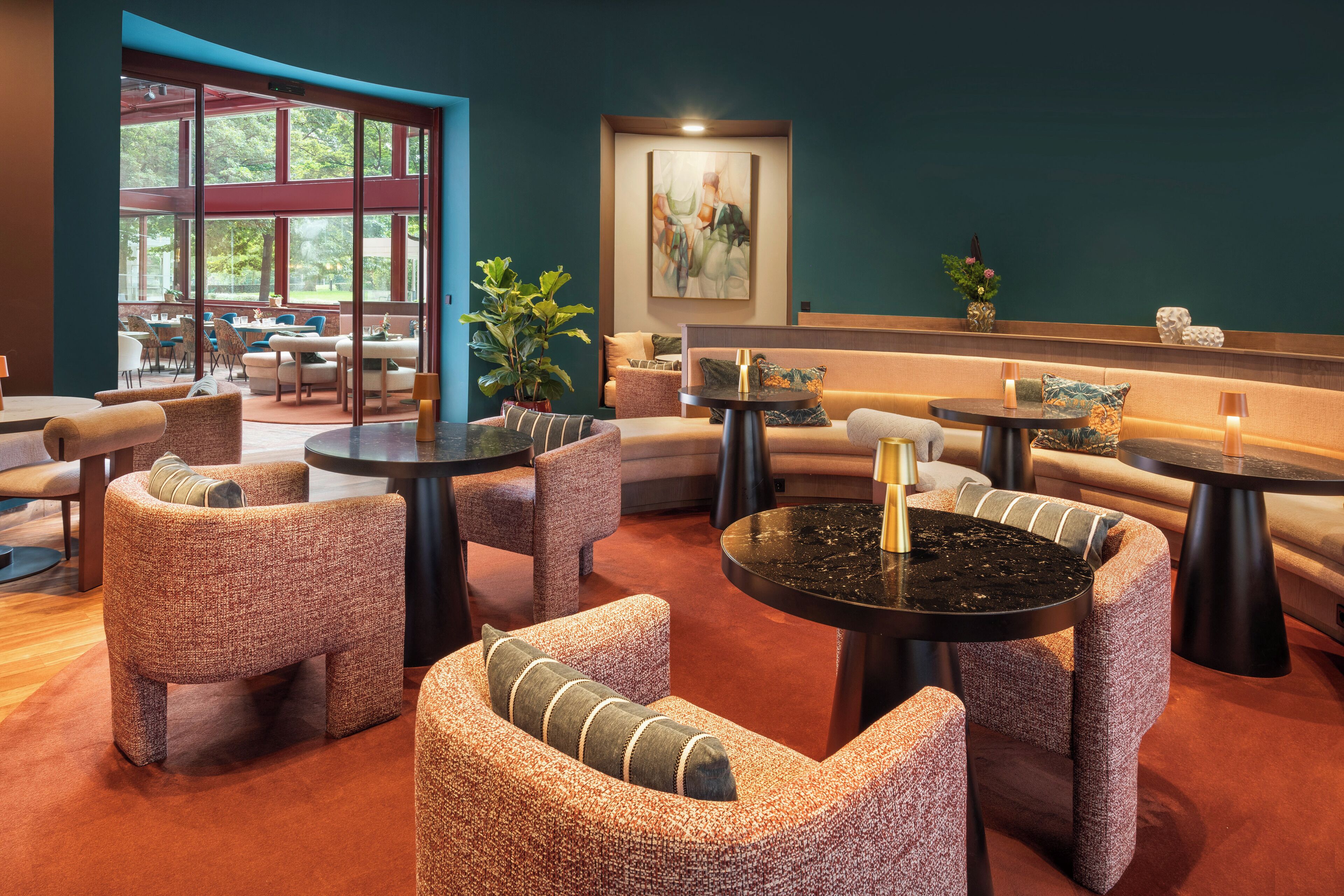 A modern lounge area with seating arrangements, tables, and a large window providing a view of the outdoors.