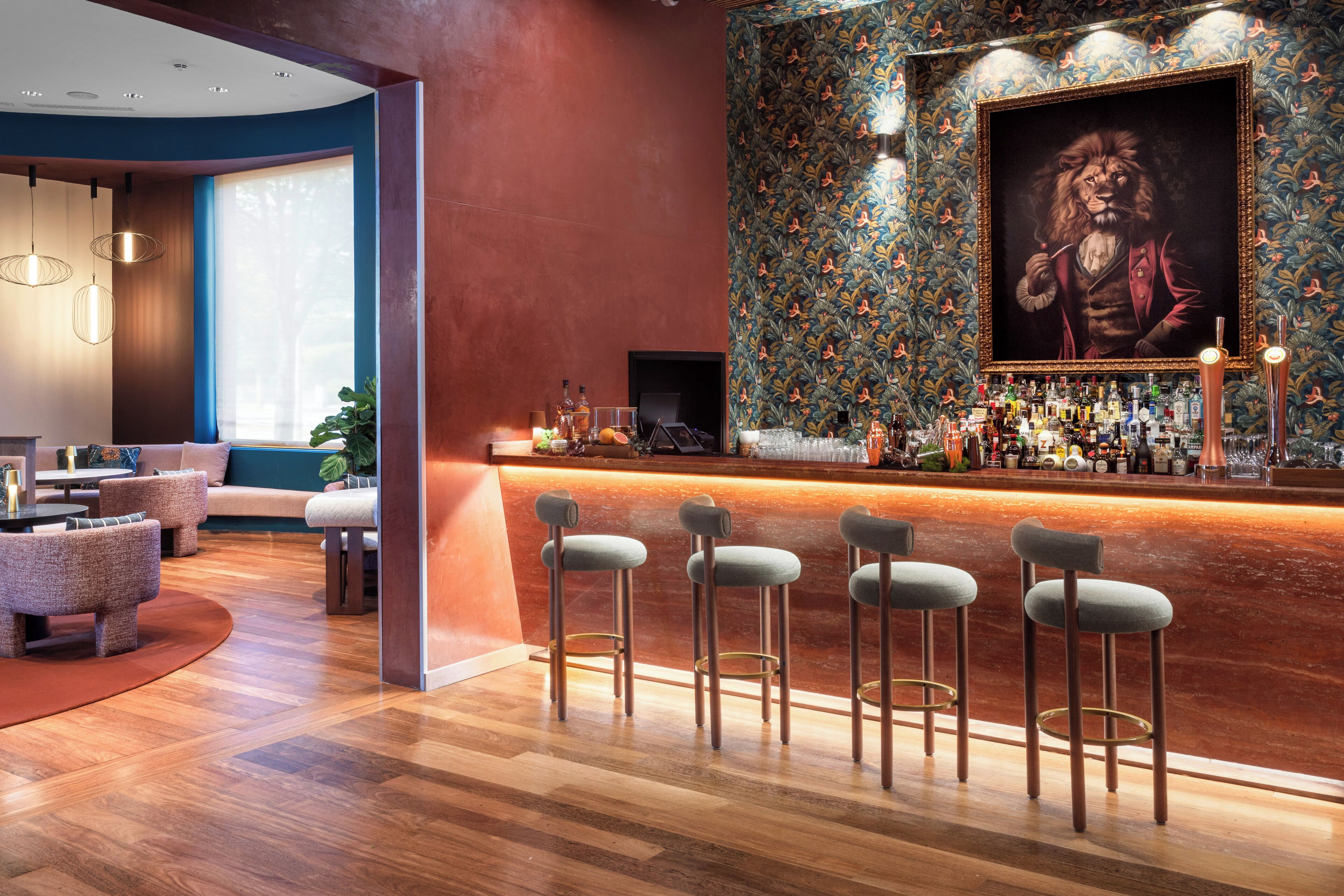 Una zona de bar con suelo de madera, taburetes y una pared con un retrato enmarcado.