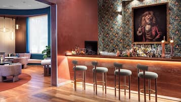 Una zona de bar con suelo de madera, taburetes y una pared con un retrato enmarcado.