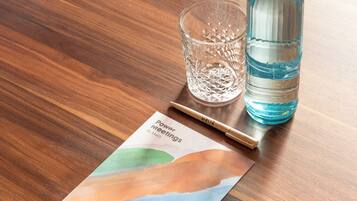 Una mesa de madera con un folleto titulado "Power Meetings", un vaso de vidrio transparente, una botella de agua azul y un bolígrafo.