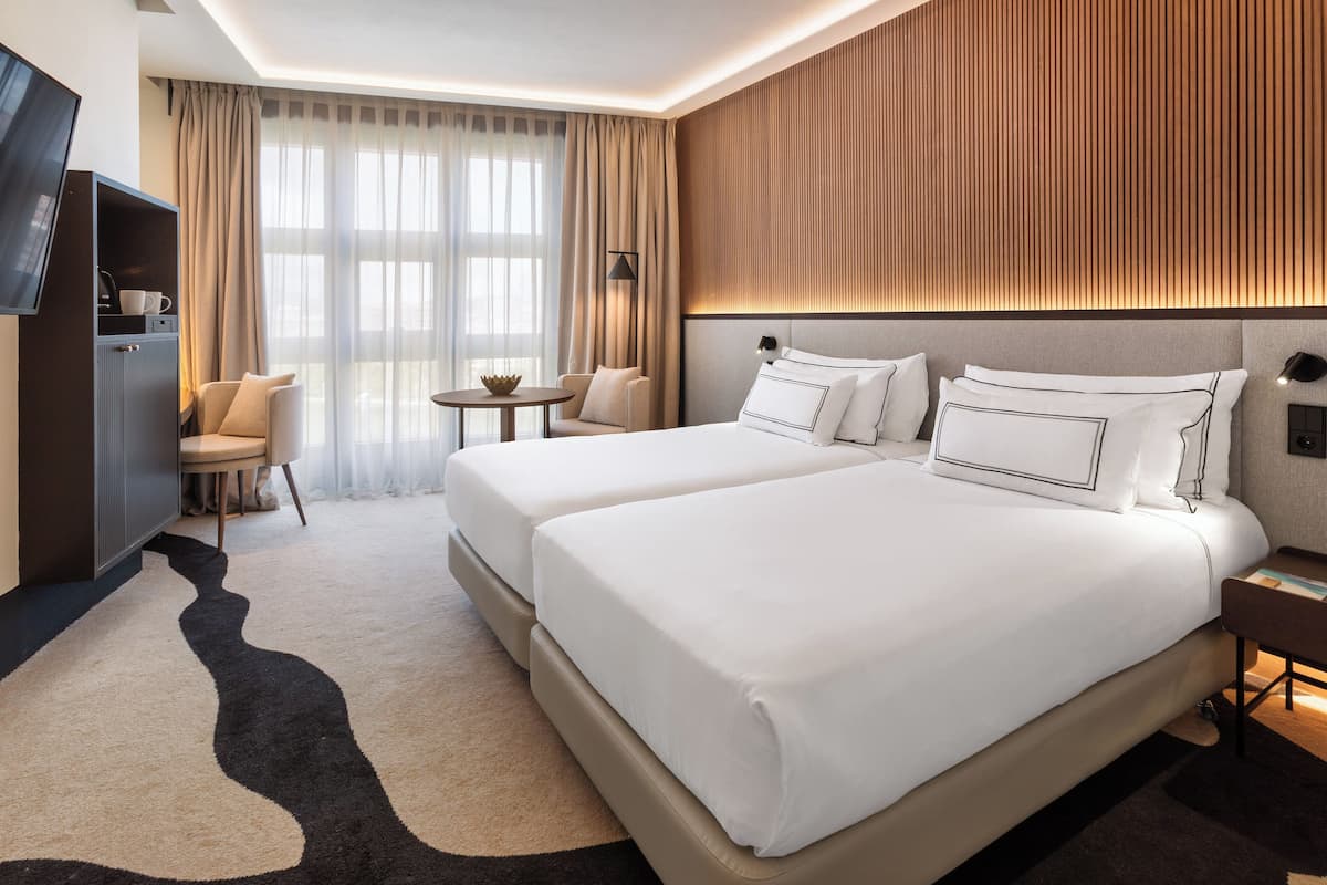 A hotel room with two beds, a TV, a desk, a chair, and a small table.