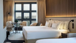 A hotel room with two beds, a small table, a chair, and a view of the city through large windows. - Hotel Melia Bilbao (Bilbao)