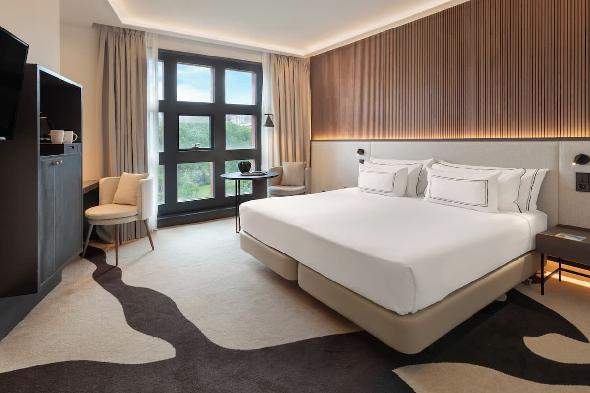 A modern hotel room with a large bed, a desk, a chair, and a television.