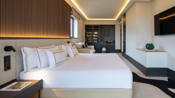 A modern hotel room with a large bed, bedside tables, a flat-screen TV, and a built-in kitchen area.