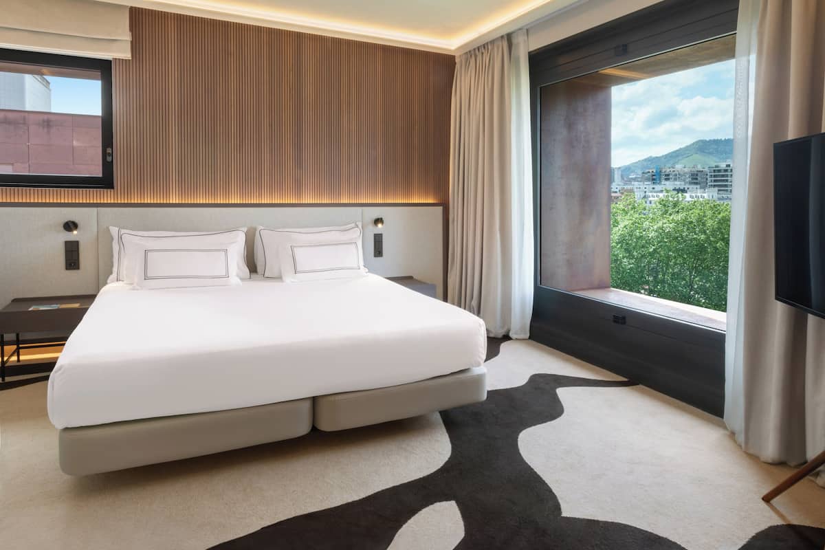 A modern hotel room with a large bed, a view of the city, and a flat-screen TV.