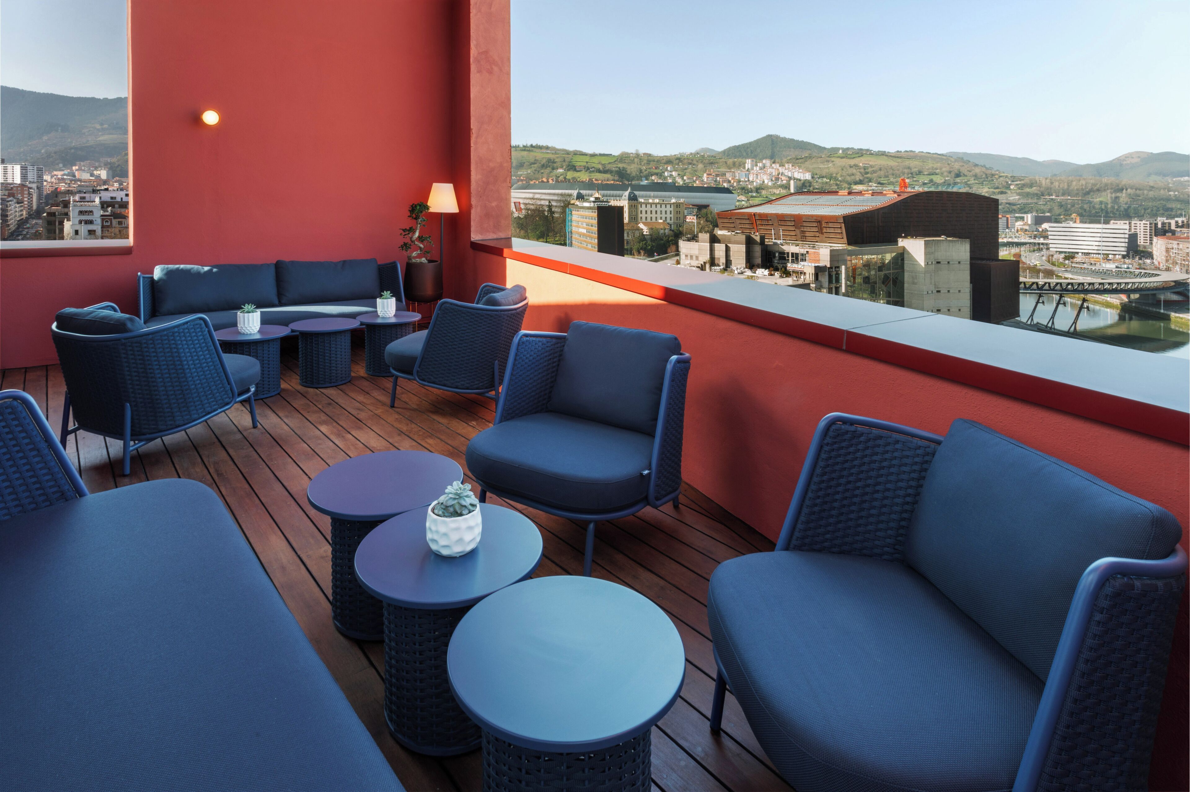 A rooftop terrace with blue seating, a table, and a potted plant.