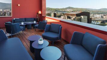 A rooftop terrace with blue seating, a table, and a potted plant.
