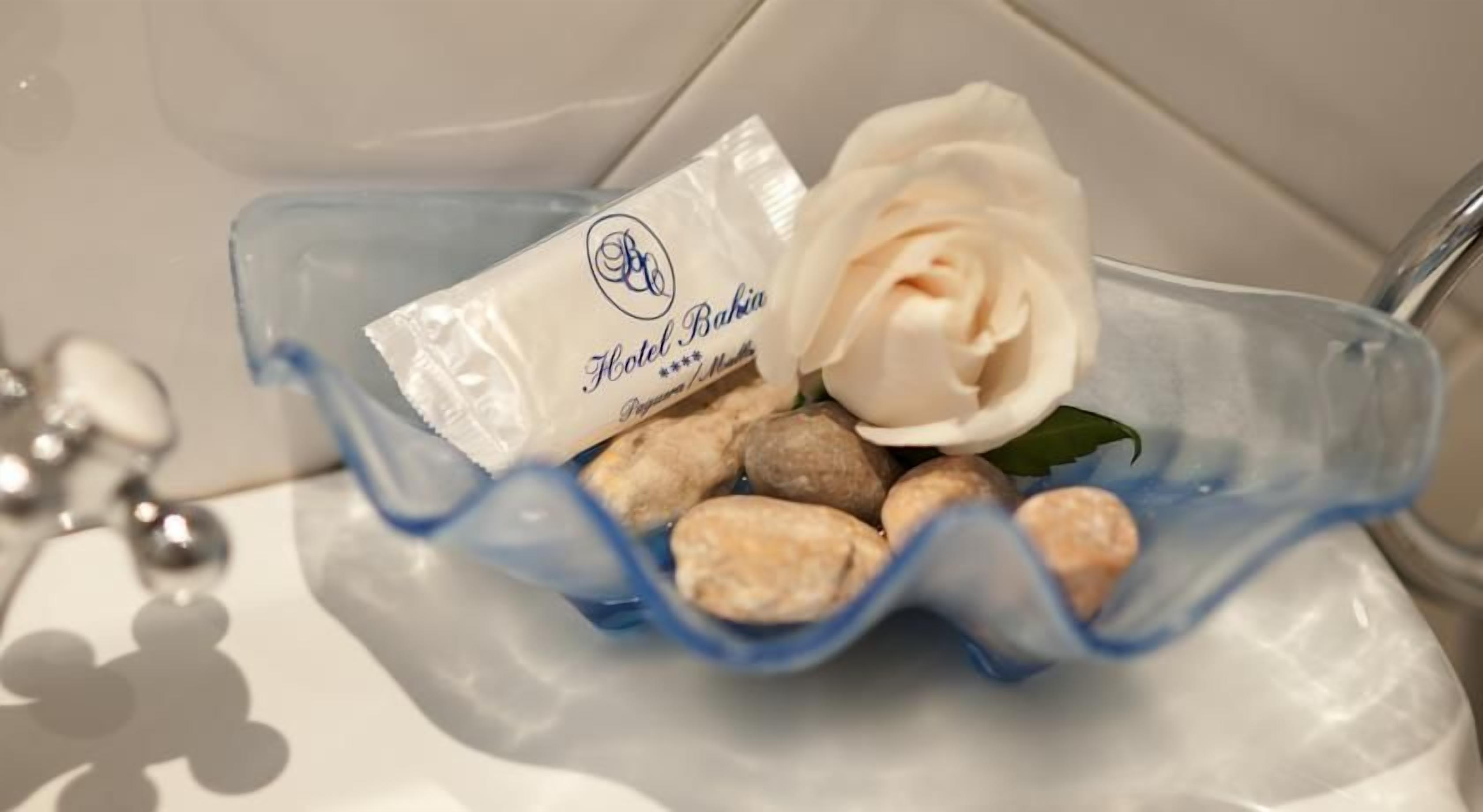A clear plastic container with a white rose and a small packet labeled 'Hotel Bahamian.'
