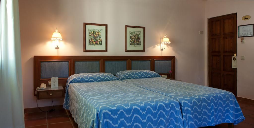 A double bed with a blue patterned bedspread, two wall-mounted lamps, and framed artwork above the bed.