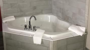 A corner bathroom with a freestanding bathtub, white tiles, and a framed artwork on the wall.