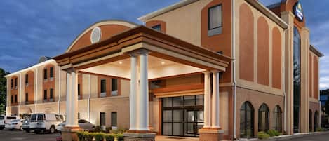 A hotel with a covered entrance, large columns, and a parking lot.