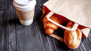 A coffee cup and a paper bag with bread on a wooden surface. - Americas Best Value Inn Holly Springs (Holly Springs)