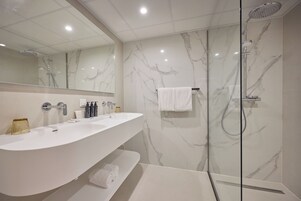 Ein modernes Badezimmer mit Marmor-Spritzschutz, einem großen weißen Waschbecken, einer Duschkabine aus Glas und einem Spiegel über dem Waschbecken.