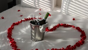Una cama con un arreglo de pétalos de rosa en forma de corazón y una botella de champán en un cubo.
