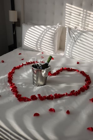 Una cama con un arreglo de pétalos de rosa en forma de corazón y una botella de champán en un cubo.