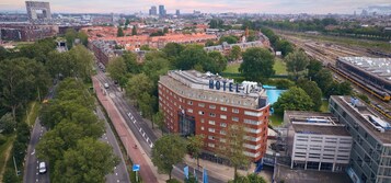 Ein Hotel mit roter Fassade in der Nähe eines Bahnhofs mit mehreren Gleisen und einer Grünanlage.