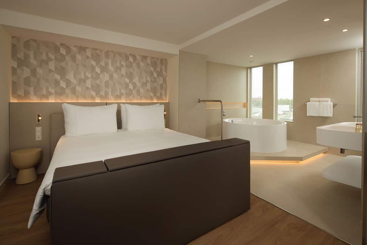 Una habitación de hotel moderna con una cama grande, un baño independiente con bañera y vistas a la ciudad.