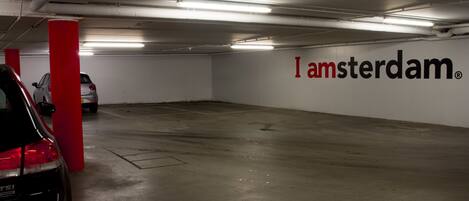A parking garage with a red pillar and a wall with "I amsterdam" text.