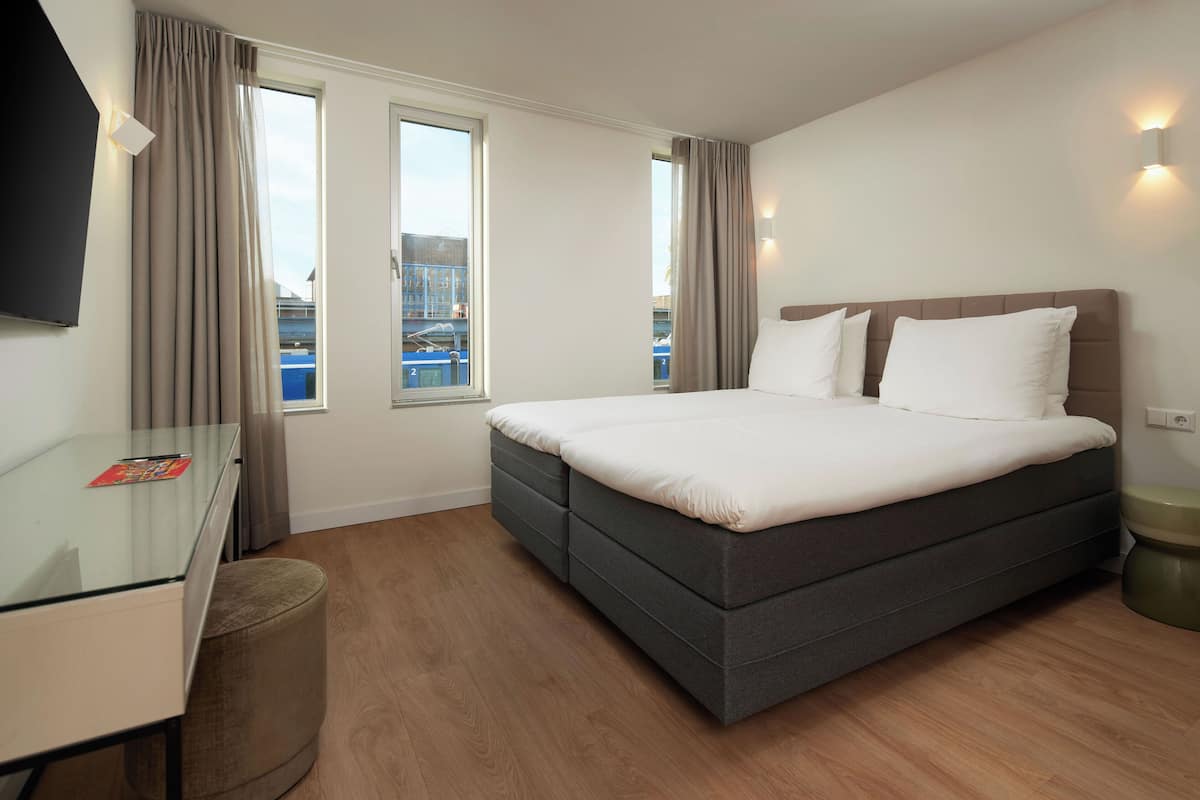 Habitación de hotel moderna con una cama grande, un escritorio de vidrio y vistas a la ciudad a través de las ventanas.