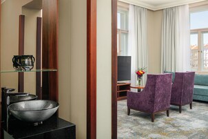 A hotel room with a large mirror, a black bowl sink, a flat-screen TV, and a purple armchair.