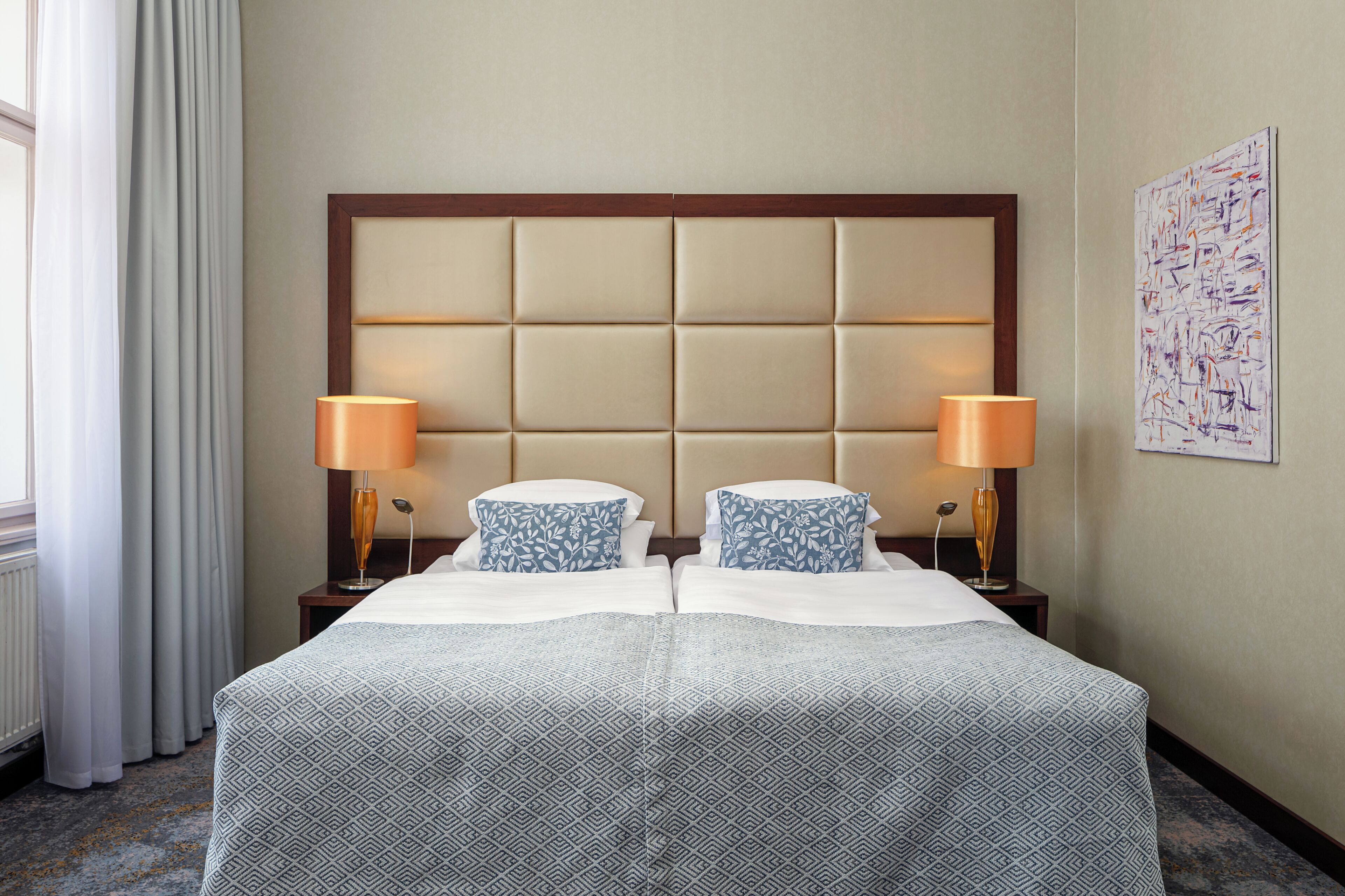 Quarto de hotel com uma cama grande, duas luminárias de cabeceira, uma cabeceira e um quadro na parede.