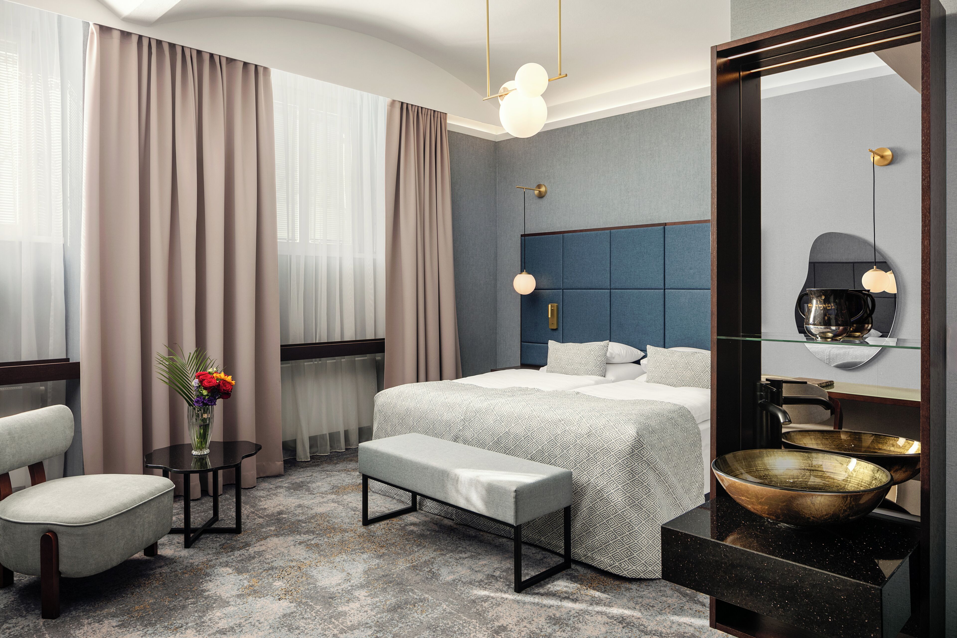 Una habitación de hotel moderna con una cama grande, una zona de estar con una silla, una mesita y un espejo amplio.