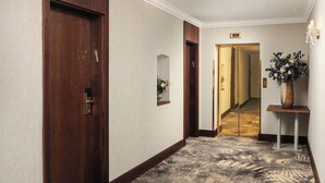 A hotel hallway with wooden doors, a carpeted floor, a mirror, a vase with flowers, and a wall-mounted light fixture. - Kosher Hotel KING DAVID Prague (Prague)