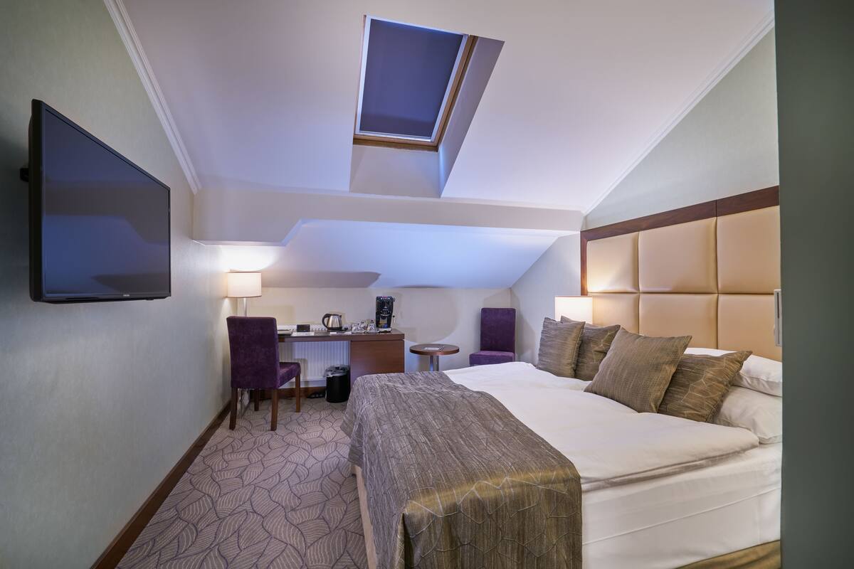 A hotel room with a bed, desk, chair, and a television.