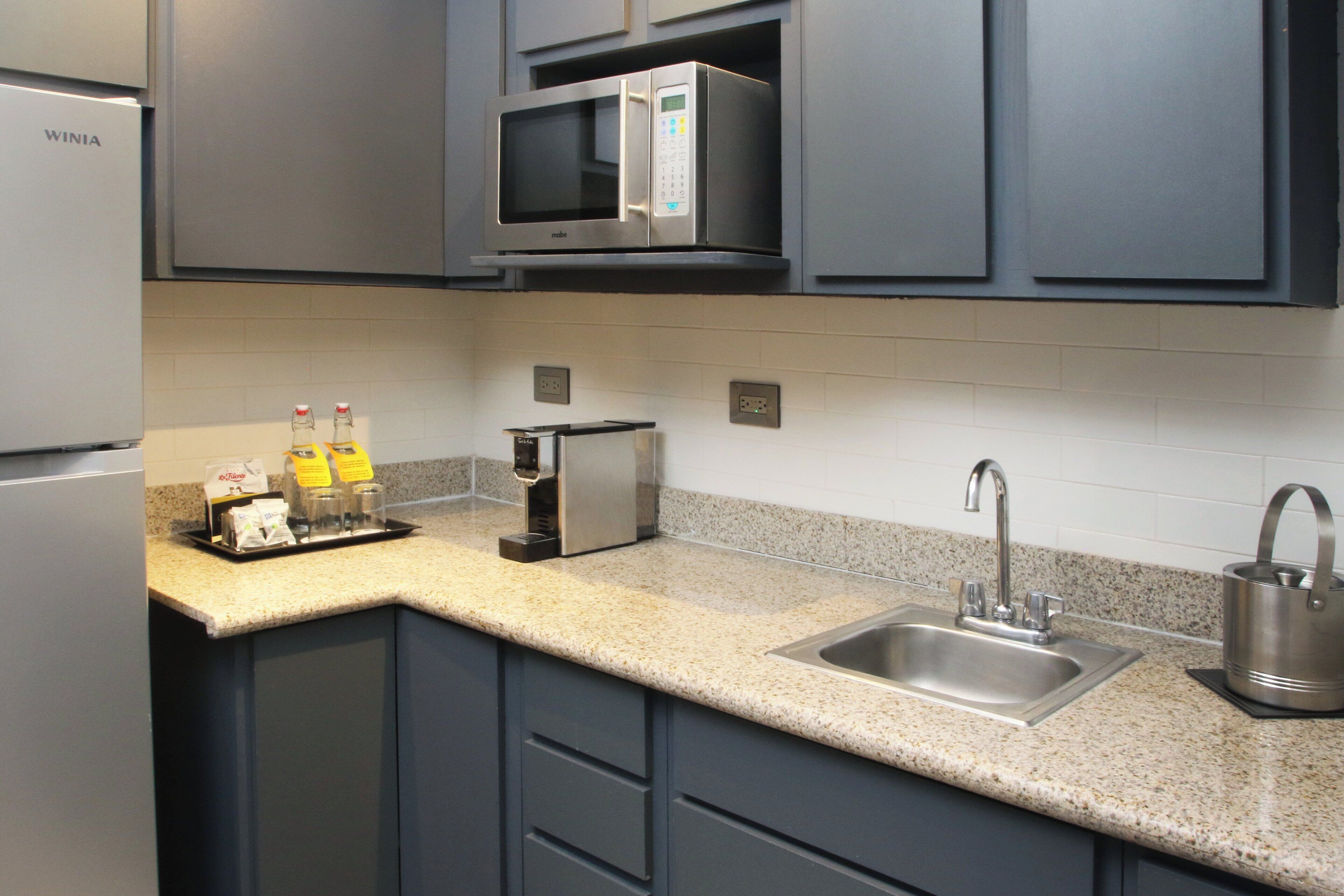 A modern kitchen with a built-in microwave, a stainless steel sink, and a kettle.