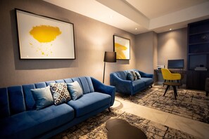 A modern living room with two blue sofas, a black floor lamp, and a yellow chair. - voco Saltillo Suites by IHG (Saltillo)