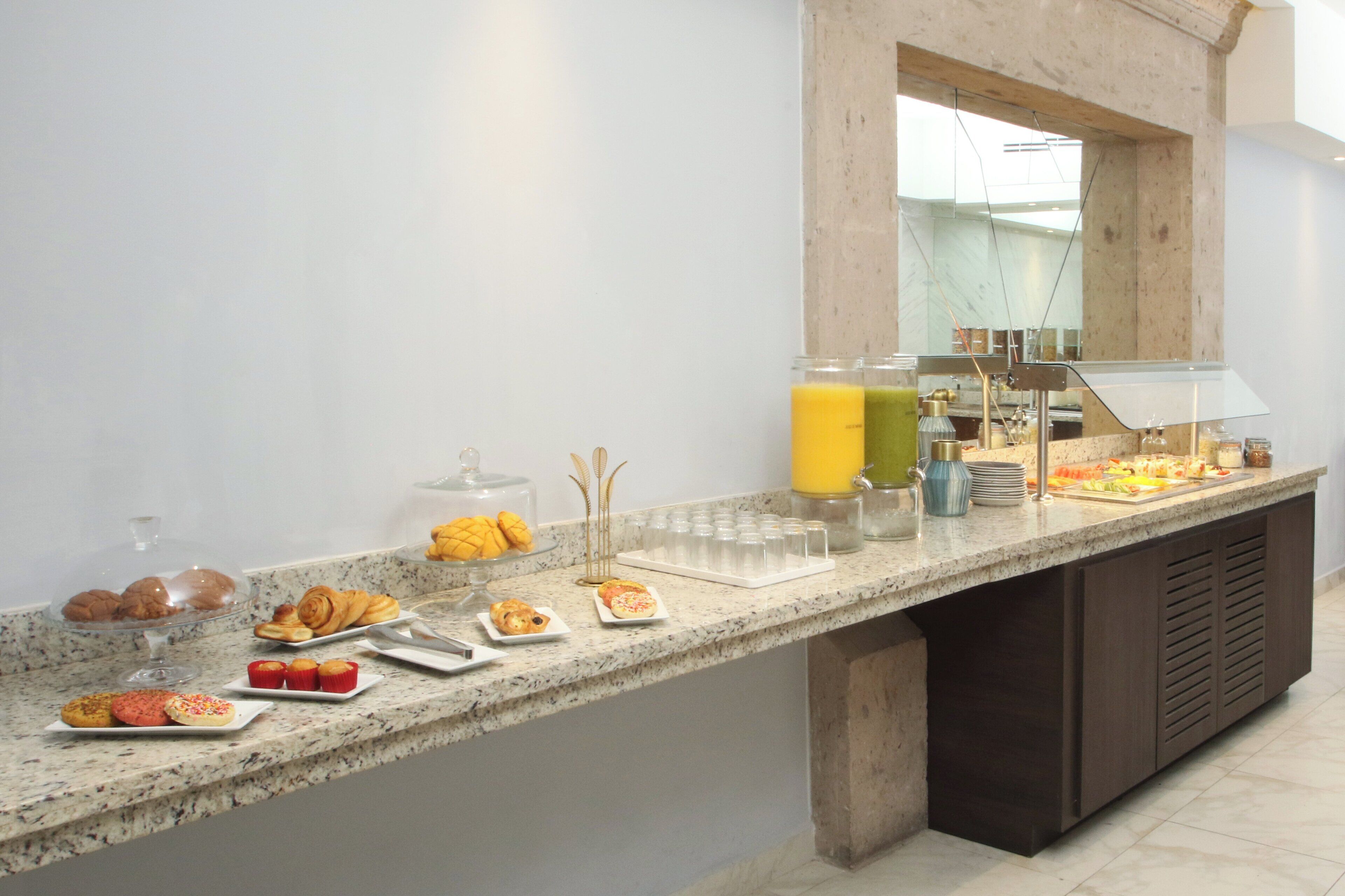 A breakfast buffet with various pastries, a juice dispenser, and a glass container.