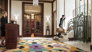 A hotel lobby with a wooden reception desk, a large floral carpet, and a grand staircase with ornate metal railings. - Hotel Juana (Antibes)