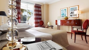 A hotel room with a bed, a desk, a chair, a lamp, and a window with curtains. - Hotel Juana (Antibes)
